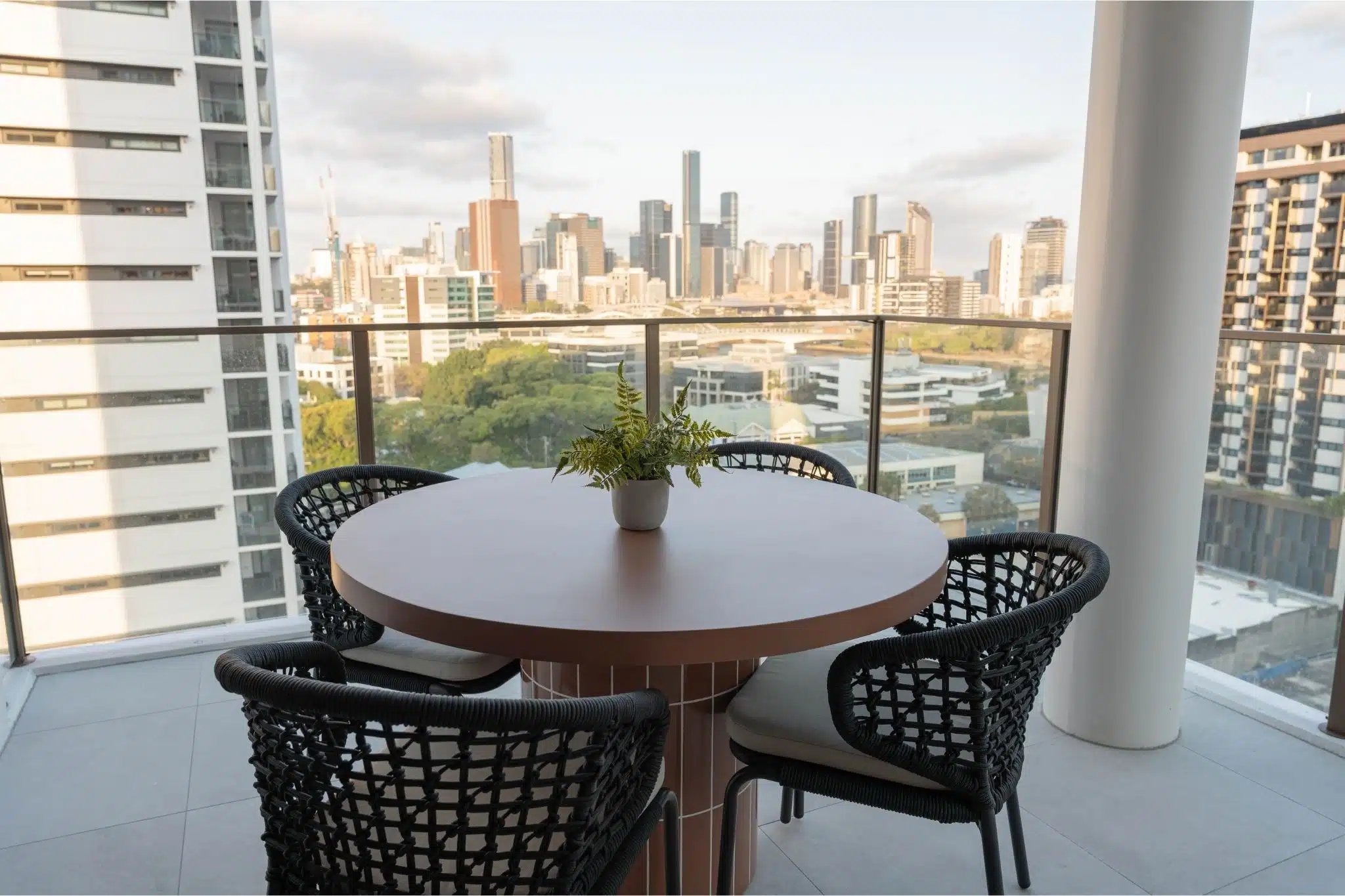 A modern table and chairs arranged on a balcony, overlooking a vibrant cityscape below.